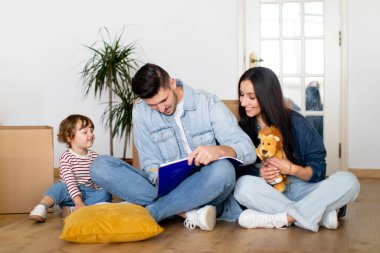 Yeni Bölüm. Çocuk taşınma gününde yerde oturan ve not defterine yazan mutlu bir aile, küçük tatlı oğlu olan genç bir çift, karton kutuların arasında dinleniyor, evi değiştirdikten sonra kontrol listesi hazırlıyorlar.