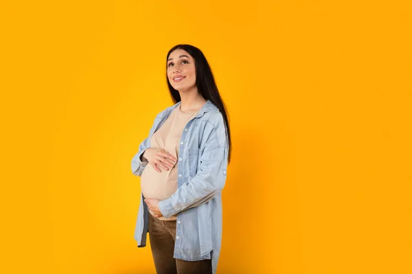 美丽的孕妇摸着肚子 幸福的未来的母亲温柔地拥抱着她的肚子和梦想 在黄色的工作室背景下享受怀孕时光 复制空间 — 图库照片