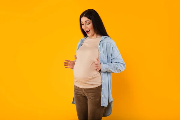 驚くべき若い妊婦感じ赤ん坊は腹の中で蹴ります 感情的に次の母親に反応します 黄色のスタジオの背景に立って — ストック写真