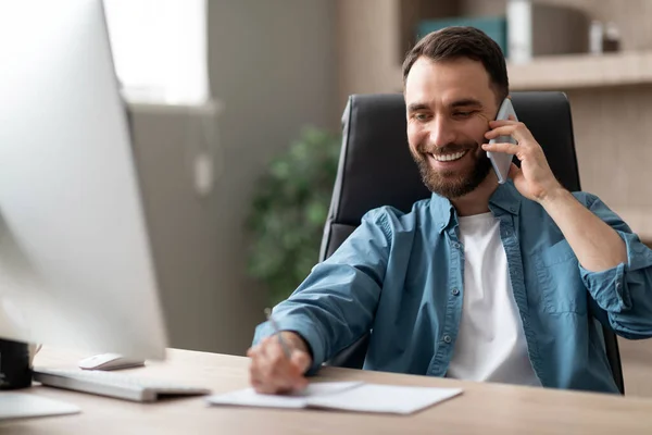Smiling Businessman Taking Notes While Having Phone Conversation Sitting Desk — Foto de Stock