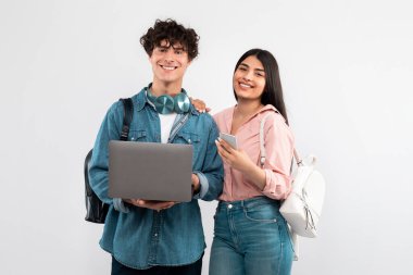 E-Öğrenme Eldiveni. Mutlu Öğrenci Çifti Laptop ve Smartphone kullanarak sırt çantasıyla Beyaz Stüdyo geçmişi üzerinde poz veriyor. Eğitimsel Web Siteleri ve Uygulamalar Reklamları