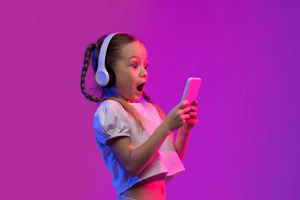 未来の背景にスマートフォンでビデオゲームをプレイし ワイヤレスヘッドフォンを使用して 携帯電話の画面を見て 目的外の感情的な驚きの少女の10代の子供 子供の娯楽やガジェット — ストック写真
