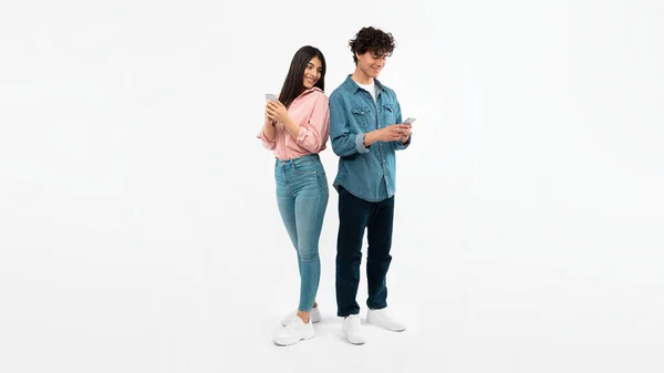 Eラーニングアプリ 携帯電話を使用して若いカップルソーシャルメディアでテキストと通信 白のスタジオの背景に立って 笑顔のガールフレンドはボーイフレンドのスマートフォンで見ています パノラマ — ストック写真