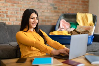 Heyecanlı İspanyol bayan dizüstü bilgisayar kullanıyor ve evde planlama gezisi yapıyor, bavulunu hazırlıyor, otel ya da uçuş biletlerini internetten ayırtıyor, tatile çıkıyor, fotokopi çekiyor.