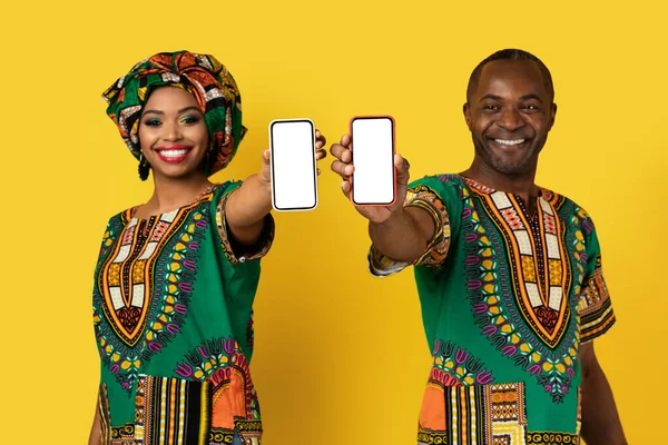 日付モバイルアプリの概念 Cheery美しいアフリカ系アメリカ人中年男性と若い女性を身に着けています民族衣装ショー携帯電話で空のスクリーンモックアップ 黄色の背景 — ストック写真