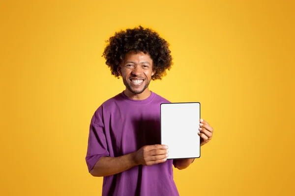 보라색 티셔츠를 곱슬머리 남자는 노란색 스튜디오에 태블릿을 프레젠테이션을 제공을 — 스톡 사진
