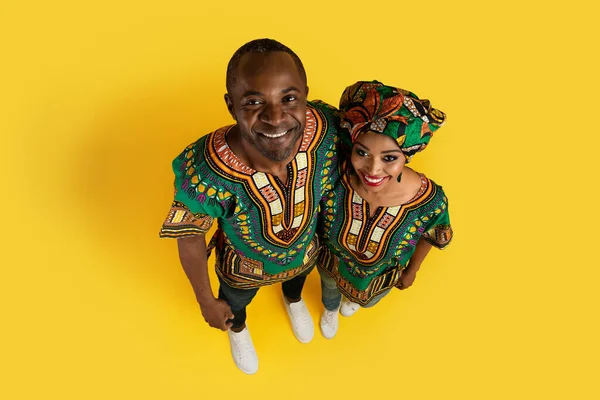 黄色のスタジオの背景にカメラで抱擁し 笑顔伝統的なアフリカの衣装を着て幸せな黒のカップルのトップビュー 愛情の概念 — ストック写真