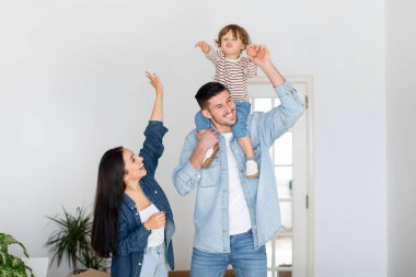 Yeni bir dairede poz veren heyecanlı, genç bir ebeveynin portresi. Üç çocuklu neşeli bir aile taşındıktan sonra oturma odasında duruyor. Mutlu bir baba çocuğunu omuzlarında taşıyor.