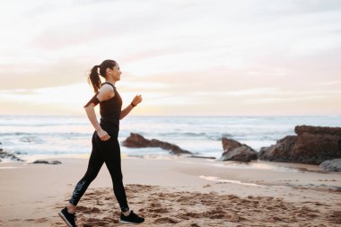 Spor giyim yarışlarında koşan neşeli, zayıf, yetişkin Avrupalı bir bayan. Sabahları deniz sahillerinde, açık havada, uzun süre antrenman yapıyor. Kas antrenmanı, kilo verme sporu, fitness ve vücut bakımı