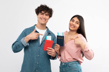 Ucuz biletler. Gülen çift biniş kartlarını gösteriyor, pasaport pozlarını beyaz stüdyo arka planında gösteriyorlar. Genç Turistler Harika Tavel Teklif Ediyor