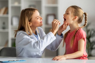 Çocuk Sağlığı Hizmetleri. Küçük kız hastasının boğazını kontrol eden kadın doktor, modern klinikte kontrol edilen tatlı bayan çocuk, anjin ya da bademcik iltihabı, streptokok, yakın çekim.