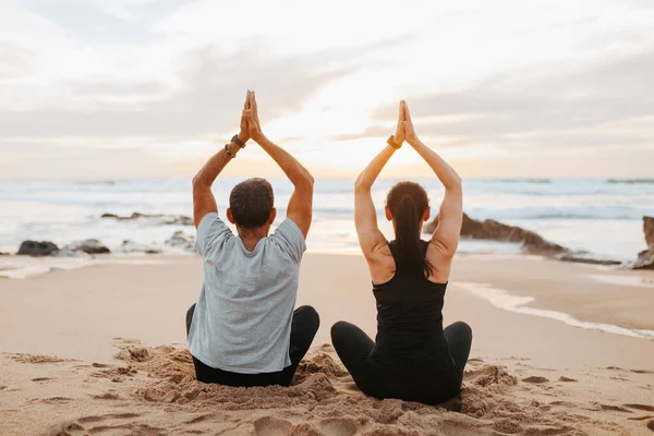 Stock image Mature european couple in sportswear practice yoga, sit, meditate, enjoy workout together in morning on sea beach, back, outdoor. Sports and peace, fitness and body care, mental health