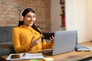 Elektronik öğrenmenin gücü. Kulaklıklı İspanyol bayan öğrenci çevrimiçi çalışmalara bağlanıyor, bilgisayar kameralarıyla konuşuyor ve el kol hareketi yapıyor. Dijital sınıf kavramı