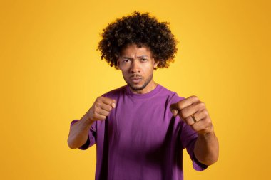 Kendinden emin, olgun, kıvırcık adam güreşçi boksör yumrukları dövüşmeye hazır sarı arka planda, stüdyoda izole bir şekilde. Ayrımcılığa karşı savaş, nefsi müdafaa ve rekabete zorlama