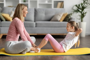 Mutlu anne ve tatlı küçük kız evde birlikte egzersiz yapıyor, sportif aile annesi ve bayan çocuk mekik çekiyorlar, oturma odasının içinde spor paspası eğitimi alıyorlar, anne destekleyici çocuk, yan görüş.