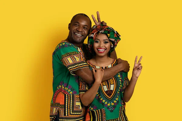 面白いです幸せな黒カップル中年男と若いです女性でカラフルな伝統的なアフリカの衣装を受け入れます ジェスチャーと笑います上の黄色のスタジオの背景 — ストック写真