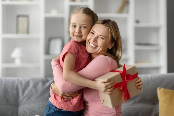 Cute Little Girl Holding Gift Box Hugging Her Mom Home — Stock Photo, Image