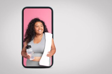 Spor kıyafetleri içinde, gri stüdyo arka planında, kolajda, boş alanda akıllı telefon ekranında bir şişe suyla büyük boy bir kadın var. Formda blog, egzersiz, kilo kaybı ve sağlık hizmetleri