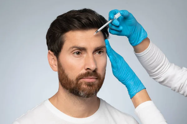 美しさを復活させる 中年男性は額のゾーンにフィラー注射を受けます 若い見て喜んで 皮膚の世話をします 灰色のスタジオの背景 — ストック写真