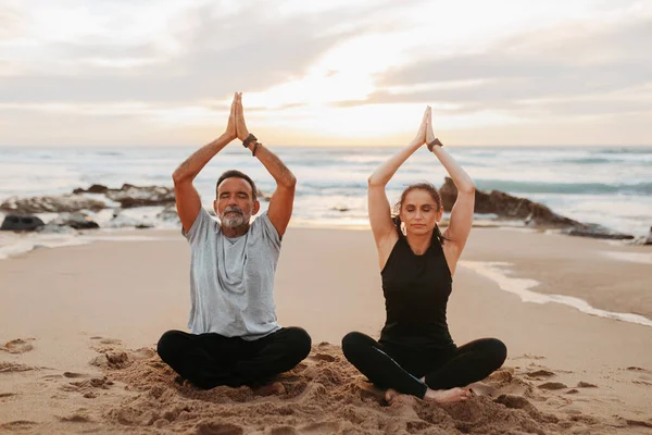 stock image Concentrated mature european family in sportswear practice yoga, meditate, enjoy workout together in morning, sit on sea beach, outdoor. Peace, sports, life style and body care, asana and breath