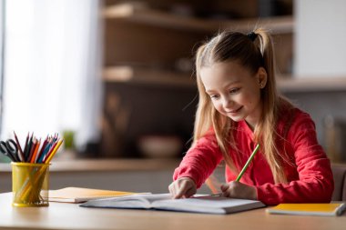 Eğitim Konsepti. Ödev yapan sevimli liseli kız, çalışma kitabında yazan gülümseyen küçük bayan çocuk, mutfak içlerinde masasında oturuyor, görev defterini kontrol ediyor, boşluğu kopyalıyor.