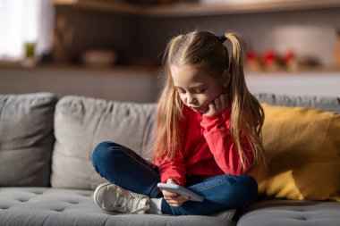 Evde koltukta dinlenirken cep telefonu kullanan küçük kız, akıllı telefonda oyun oynayan ya da internette gezinen genç kız, yeni uygulamaları kontrol eden üzgün çocuk, boşluğu kopyalayan