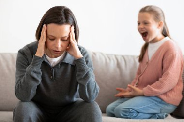 Unhappy caucasian middle aged mother suffers from screams and whims of daughter in living room interior. Relationship problems at home, parenting, scandal and stress with troubled teenager clipart