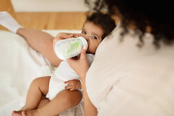 Black Millennial Mother Feeds Bottle Hungry Little Baby White Bed — Stock Photo, Image