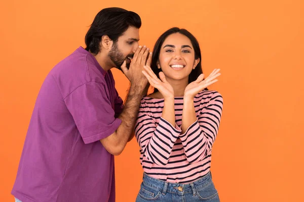 ハンサムな若いインド人男性共有秘密や噂とともに彼の感情的な可愛いですガールフレンド 明るい東カップルでカジュアルな衣装で一緒にポーズオレンジ色のスタジオ背景 コピースペース — ストック写真