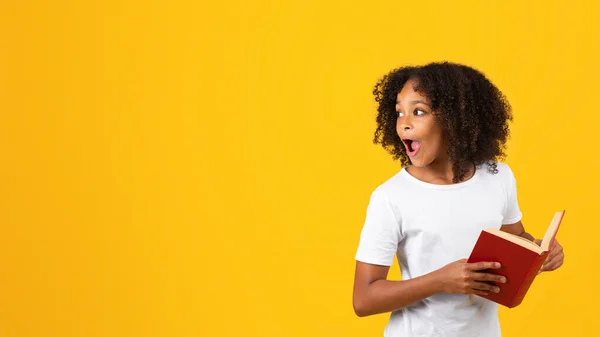 明るくショックを受けたのは 白いTシャツを着た10代の黒人の少女で 開いた口と本が空の空間を見て 黄色のスタジオの背景に孤立している オファー — ストック写真