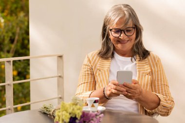 Gülümseyen beyaz saçlı, gözlüklü yaşlı kadın kafeteryada bir buketle oturuyor, bir fincan kahveden hoşlanıyor ve dışarıda akıllı telefondan mesaj okuyor. Bayan uygulamayı sever, dinlenir ve dinlenir, boş zaman