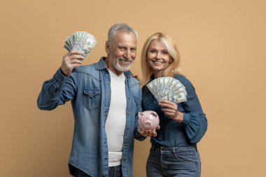 Mutlu, güzel, yaşlı çift ellerinde nakit para, kumbaralar ve renkli stüdyo geçmişlerinde izole edilmiş kumbaralar tutuyorlar. Tasarruf, mevduat, emeklilik sırasında finansal okuryazarlık