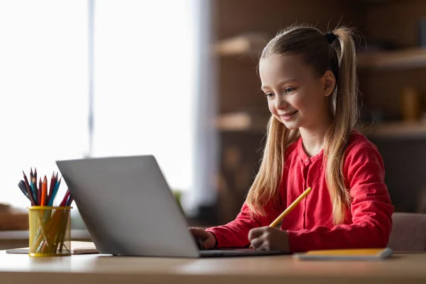 可爱的小白种女孩在家里用笔记本电脑学习 在记事本上写字 在厨房里微笑着坐在餐桌旁 用电脑学习 享受网上教育 — 图库照片