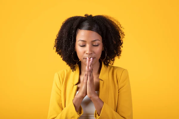 静下心来 年轻的黑人女士闭上眼睛祈祷 和平的女人手牵着手沉思 站在黄色的工作室背景上 信仰概念 — 图库照片