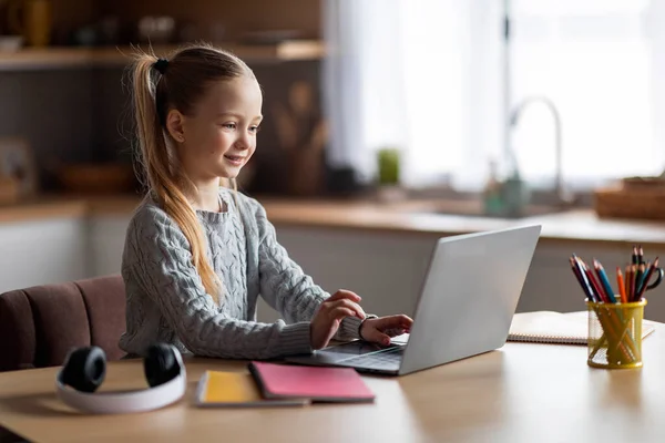 为儿童编写代码 可爱的小女孩坐在桌边用笔记本电脑 微笑着参加编程课程 看电脑屏幕 在键盘上打字 — 图库照片