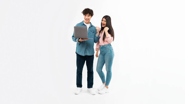 Digital Victory. Joyful Young Couple With Laptop Shaking Fists Celebrating Great Online News Browsing Internet Together Standing Over White Studio Background. E-Learning Success. Panorama