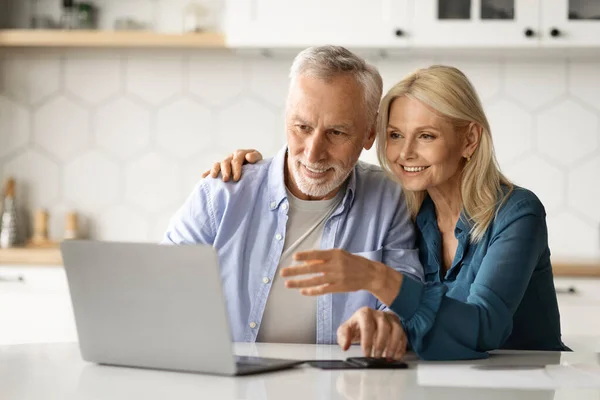 Happy Senior Couple Paying Taxes Online With Laptop In Kitchen, Smiling Elderly Spouses Using Computer At Home, Planning Family Budget Together, Accounting Expenses, Closeup Shot With Free Space