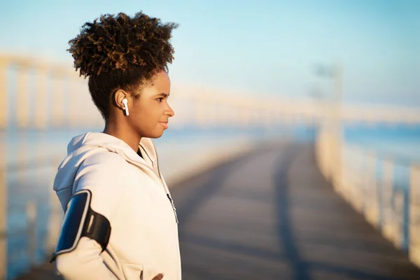 stock image Sporty Young Black Woman With Armband And Earphones Standing Outdoors, Motivated African American Female In Sportswear Getting Ready For Morning Run Or Outside Workout, Side View With Copy Space