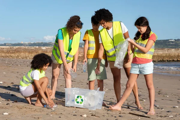 忙碌而积极的国际青少年志愿者身着制服 在箱子里收集垃圾和塑料瓶 在海滩上循环利用 保护海洋 保护环境 清理地球 — 图库照片