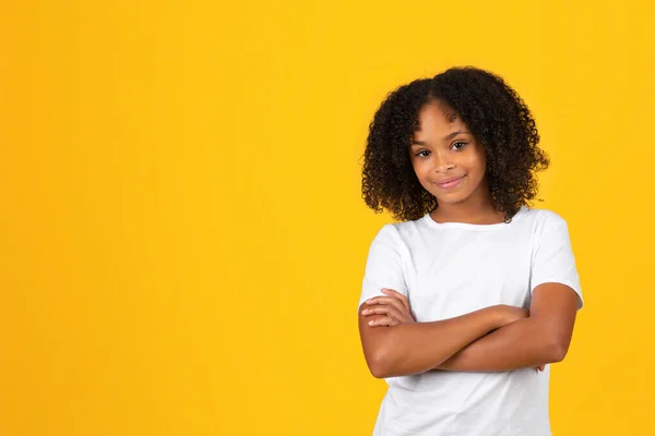 微笑着自信的青春期卷曲女孩穿着白色的T恤 胸前交叉的胳膊 孤立的黄色工作室背景 在学校 广告和广告中学习和教育学生的情感 学习和教育 — 图库照片