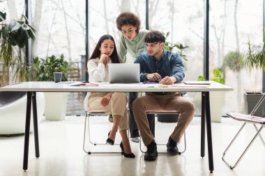 İş sorunları çözme. Üç etnik çeşitlilikte iş arkadaşından oluşan bir ekip laptopun modern ofiste çevrimiçi açılışıyla ilgili sorunları var. Zor Görevde Birlikte Çalışan Ciddi Genç Meslektaşlar