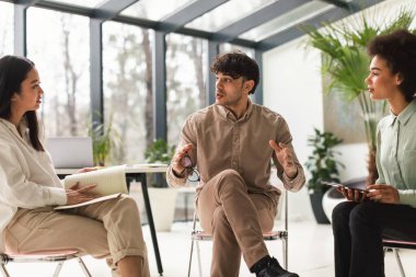 Takım çalışması ve takım oluşturma. Genç Çok Kültürlü Meslektaşlar Üçlüsü Başarılı Takım Çalışması Yapıyor Sandalyelerde oturuyor, Modern Ofiste Şirket Toplantısı sırasında Girişimleri tartışıyor