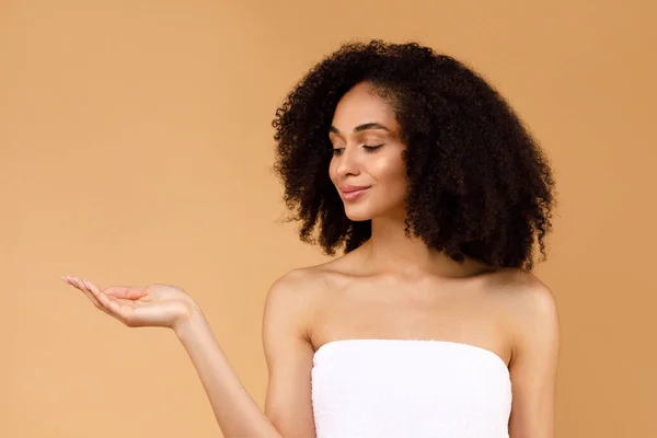 目に見えないオブジェクトを保持忙しい髪を持つ美しい黒の女性 オープン手のひらで立って 新しい美しさの製品をお勧めします ベージュのスタジオの背景の上にポーズ モックアップ バナー — ストック写真