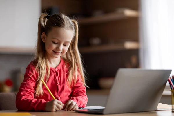 stock image Adorable Little Girl Writing Notes While Study With Laptop At Home, Cute Preteen Female Child Doing School Homework Or Noting Information From Internet, Sitting At Desk In Kitchen Interior