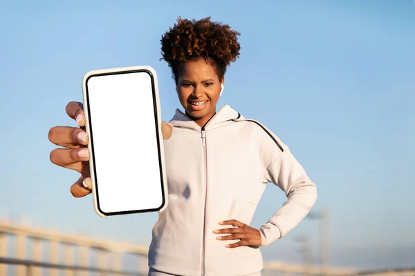 惠康应用 穿运动服的年轻非洲裔美国女士用白色屏幕展示手机 推荐移动应用 — 图库照片