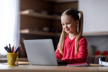 Evde eğitim. Gülümseyen ergen kız evde dizüstü bilgisayarla ders çalışıyor, küçük tatlı kız bilgisayar başında eğitim platformunu kullanıyor, mutfakta iç kısımda oturuyor, çevrimiçi öğrenmenin keyfini çıkarıyor.