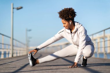 Sportif Siyah Kadın Portresi Açık havada antrenman yaparken kaslarını esnetiyor, Atletik Afrikalı Amerikalı kadın koşmadan önce ısınıyor, Denize yakın tahta iskelede egzersiz yapıyor, Uzay Kopyasını yapıyor.