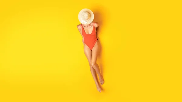 穿着夏帽和一件橙色泳衣的女人放松和晒日光浴躺在黄色工作室的背景下 从上方看 泳衣及时装横幅 — 图库照片