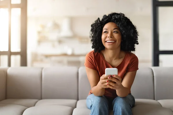 Hayalperest Genç Siyah Kadın Elinde Akıllı Telefonuyla Koltukta Oturuyor Uzaklara — Stok fotoğraf