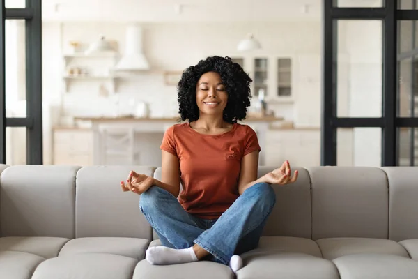 Sakin Siyah Kadın Kanepeye Oturmuş Evde Gözleri Kapalı Meditasyon Yapıyor — Stok fotoğraf